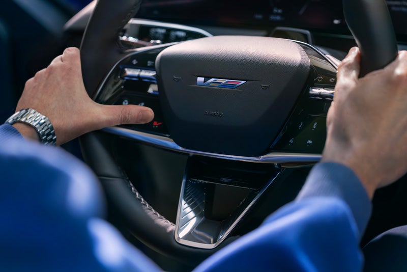 Close-up of a Man About to Press the V-Button on the 2026 OPTIQ-V Steering Wheel | Coughlin Cadillac Marysville in Marysville OH